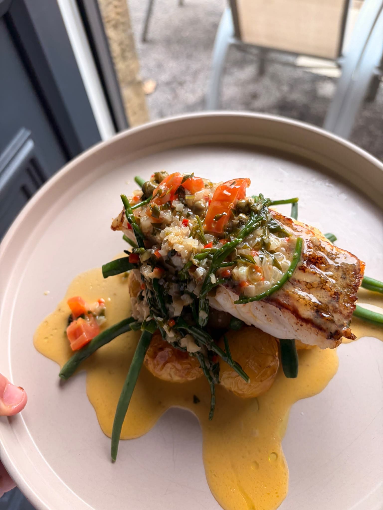 A grilled fish fillet topped with capers, tomato and samphire, on green beans and new potatoes