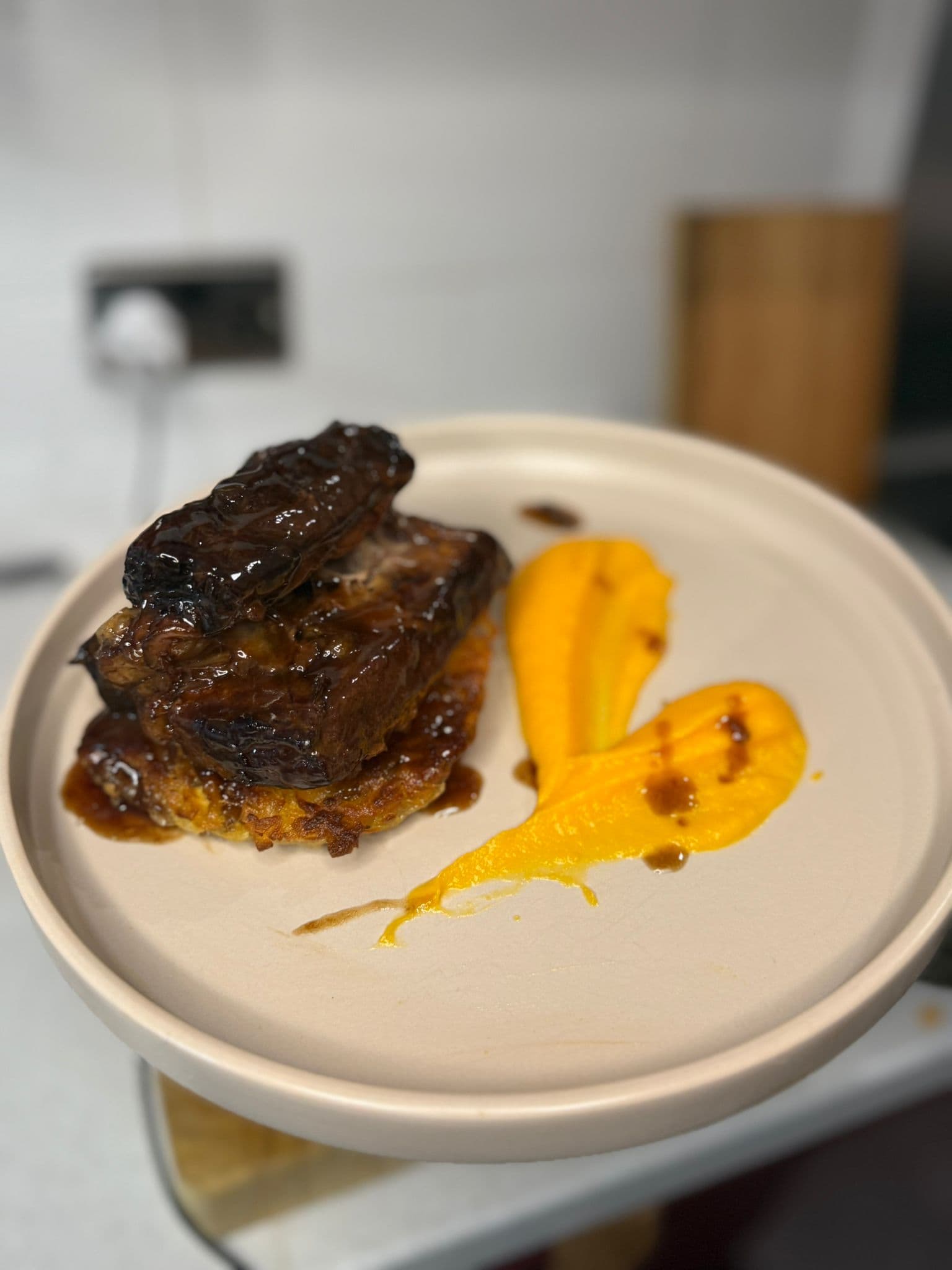 Glazed braised meat on a crisp potato cake with a bright orange purée