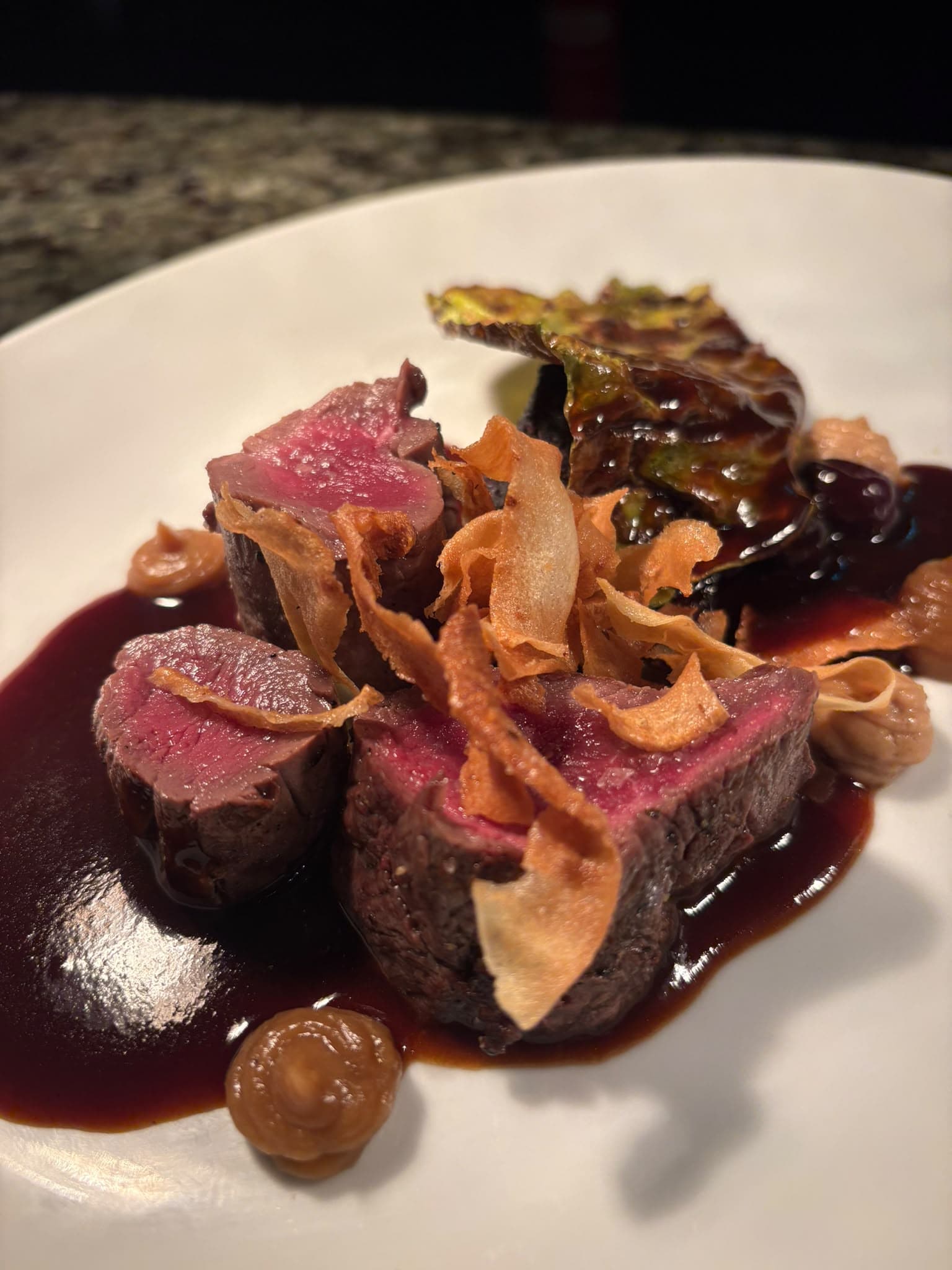Sliced rare fillet with crisp shavings, a glossy dark sauce and a charred cabbage leaf