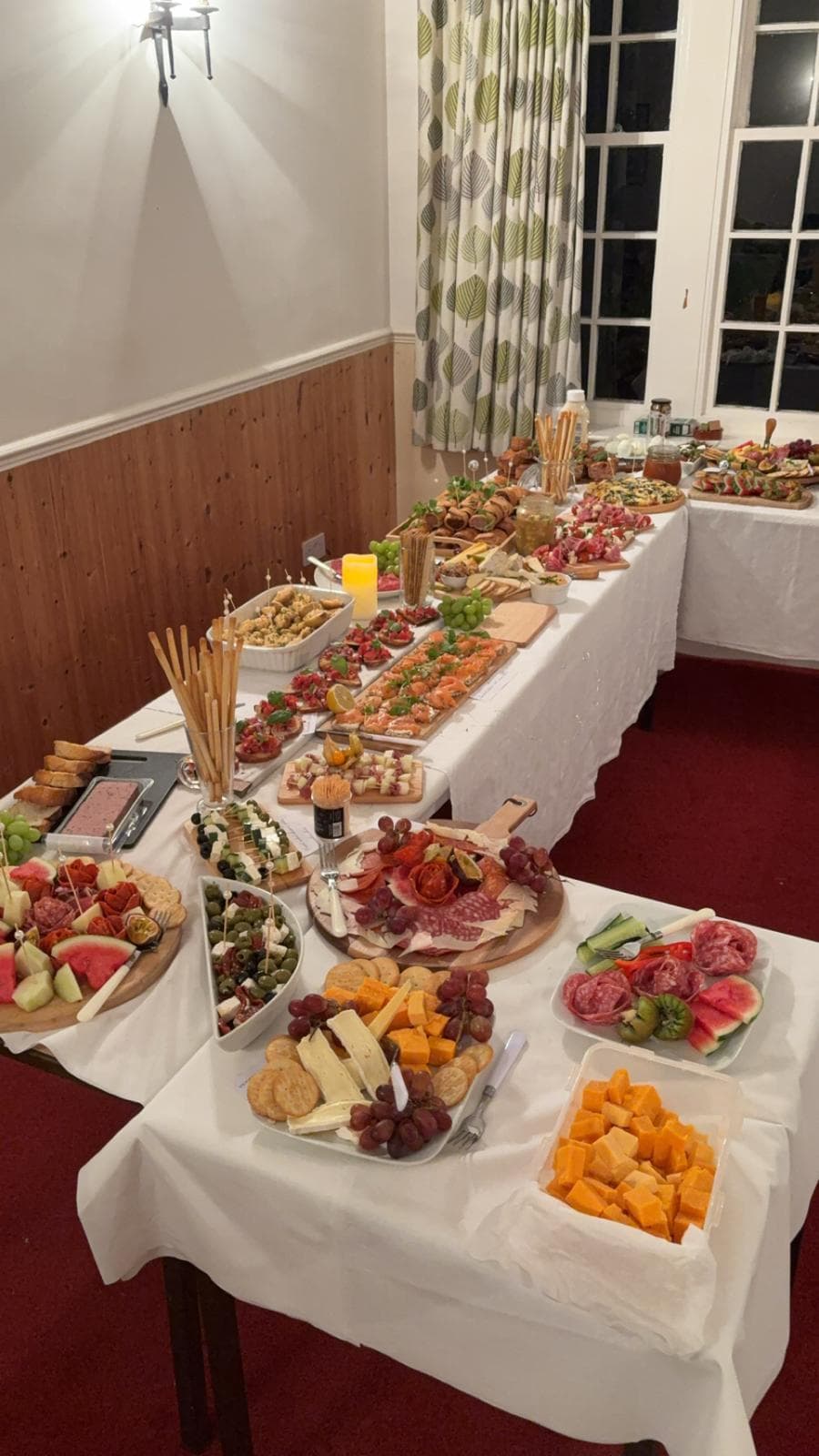 A long buffet table laid with platters of cured meats, cheese, fruit, bruschetta and smoked salmon