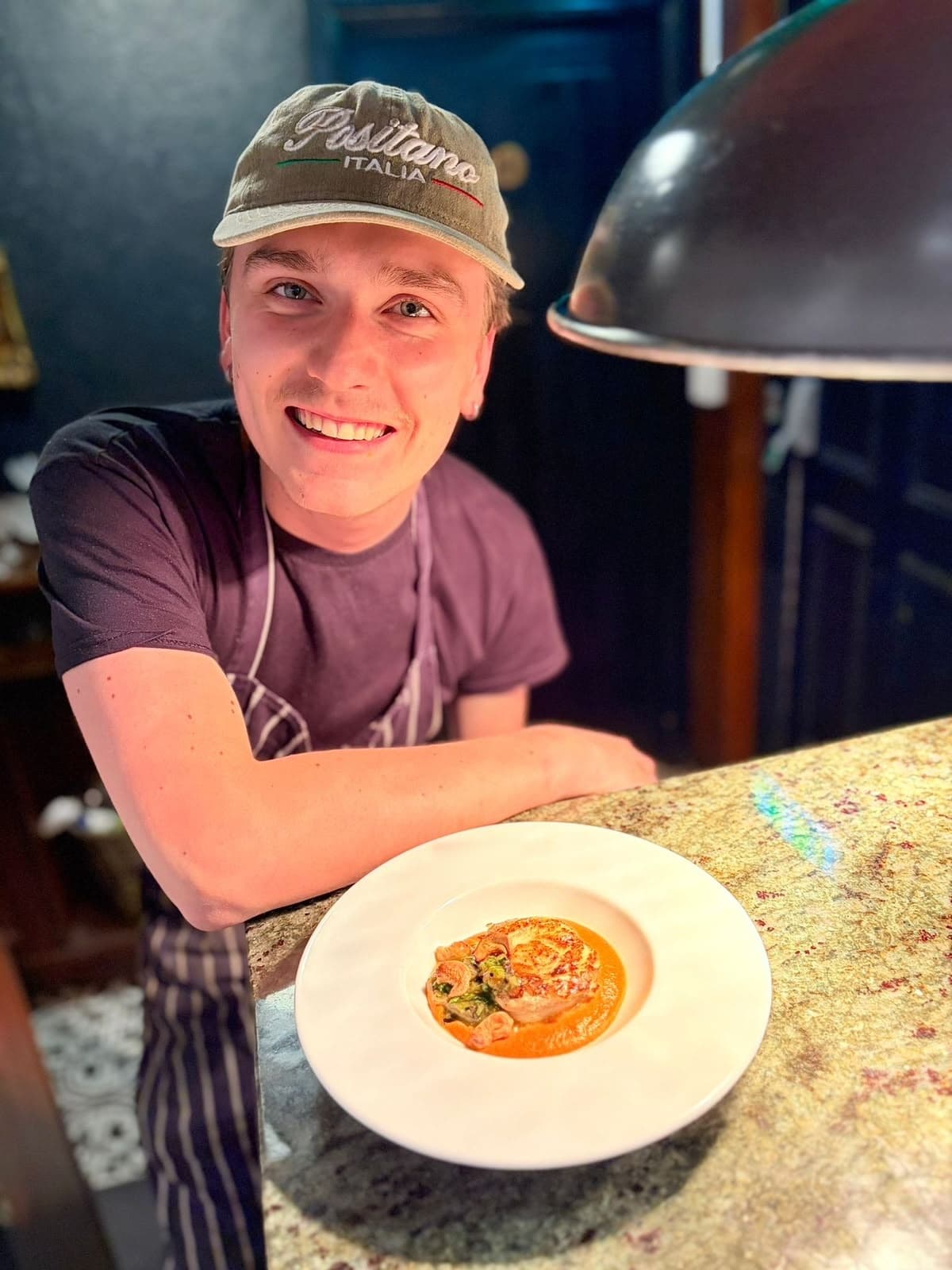 Louie smiling at the pass, leaning on the counter beside a plated dish