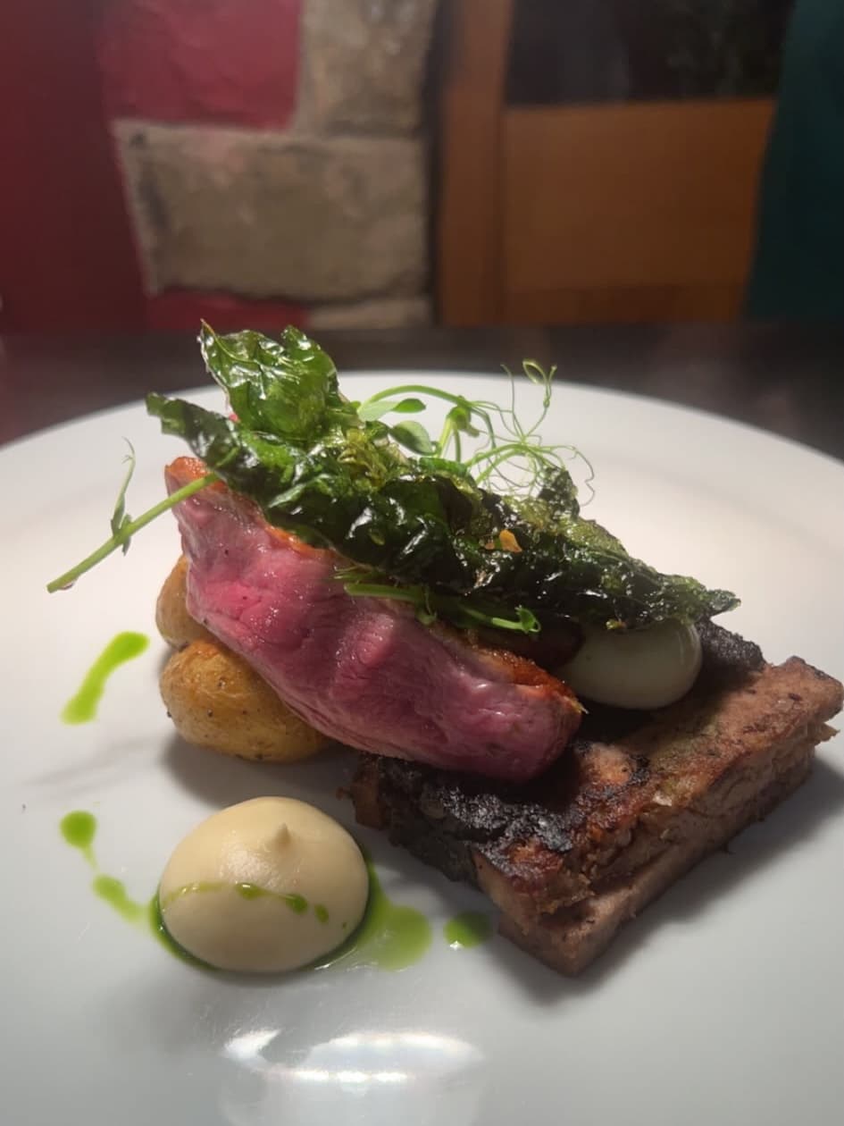 Pink beef topped with crisp greens and pea shoots, with roast potatoes, a purée and herb oil