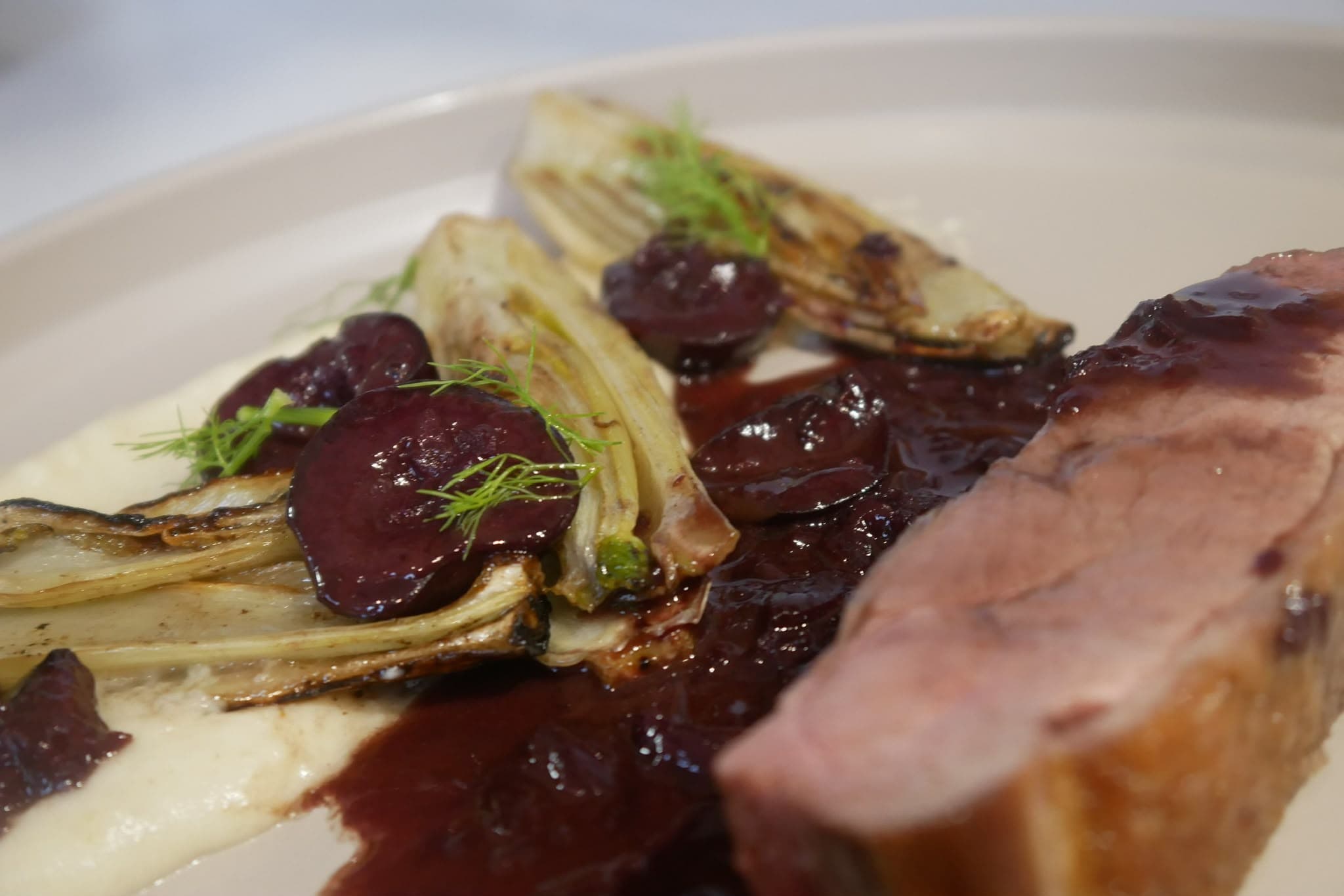 Slices of pink roast meat with charred fennel, dark fruit and a smooth white purée