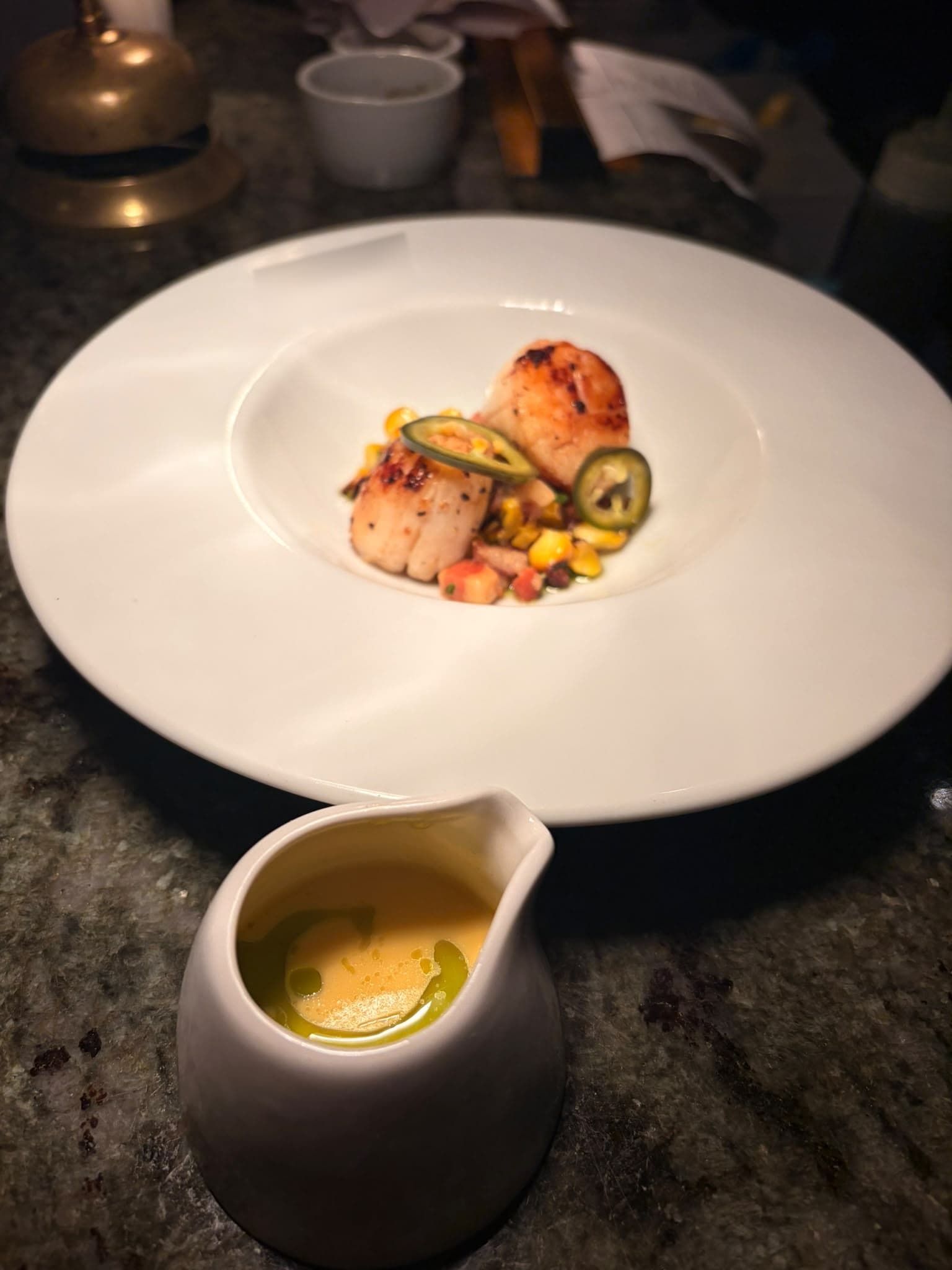 Two seared scallops on a sweetcorn and chilli salsa, with a small jug of sauce