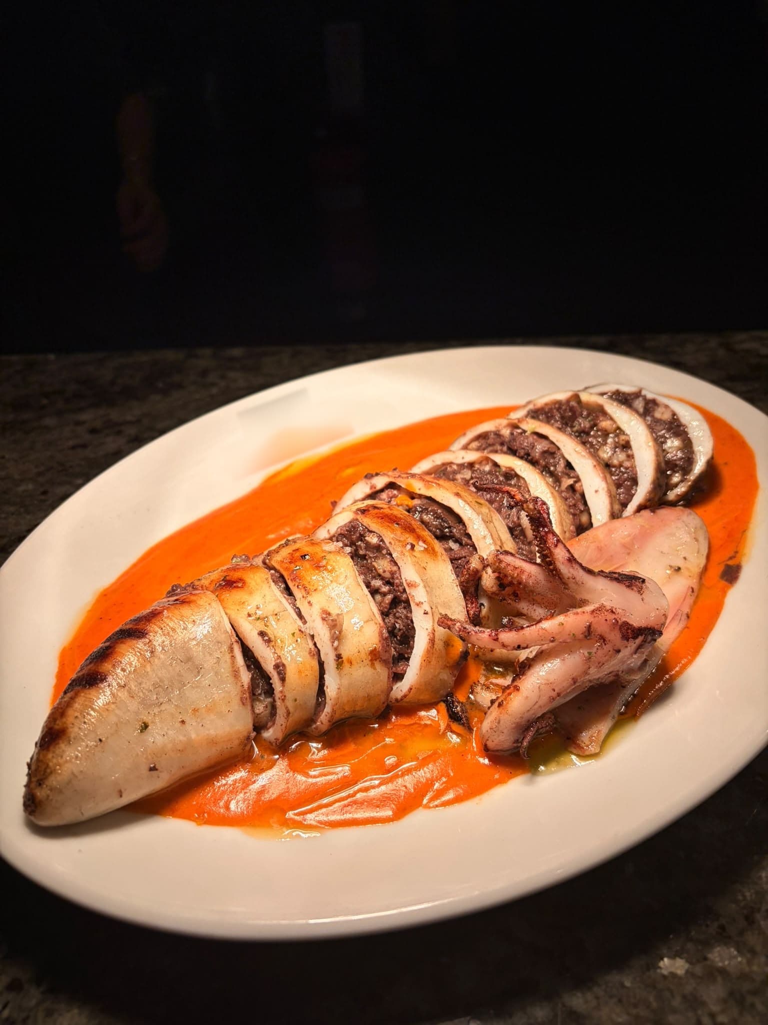 A whole stuffed squid, sliced and grilled, on a bright orange sauce