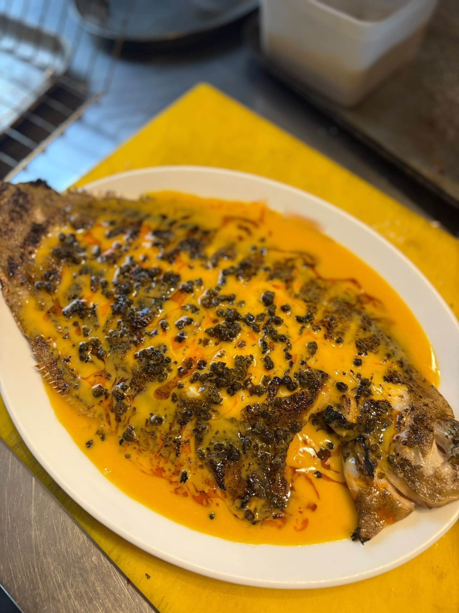 A whole grilled flatfish covered in a golden butter sauce and crispy capers